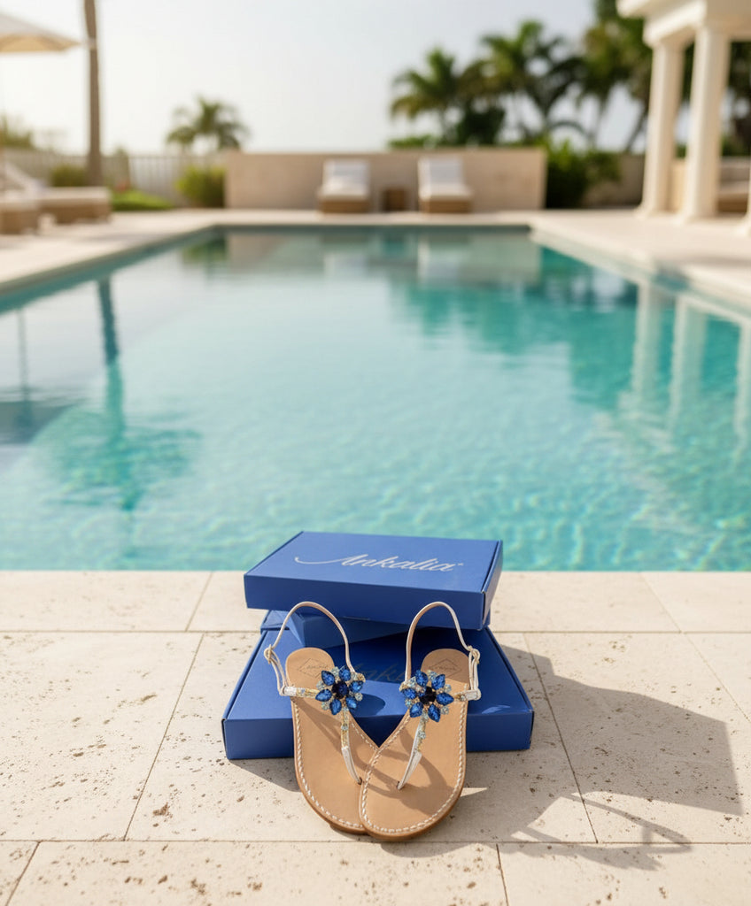 Pair of white sandals with blue Swarovski crystal embellishments in front of a luxury blue box.