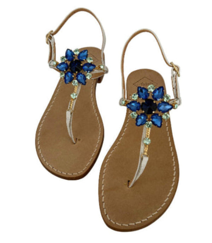 Pair of white sandals with blue flower embellishments on a white background
