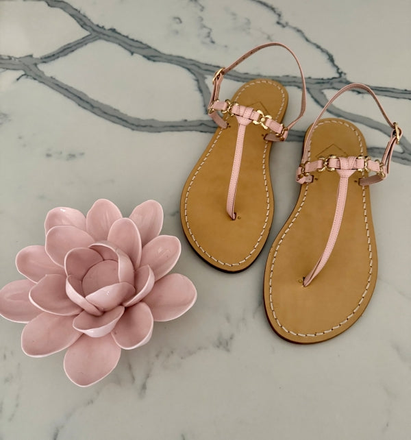 Pair of pink leather sandals on a marble surface with a pink flower.