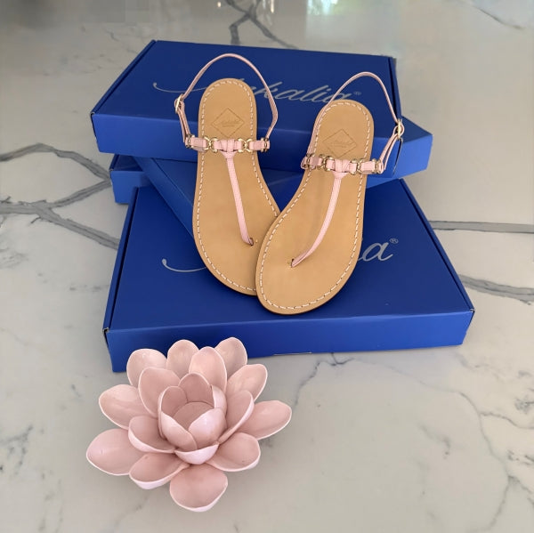 Pair of pink leather  sandals on Ankalia luxury blue packaging, accompanied by a pink flower on a marble surface.