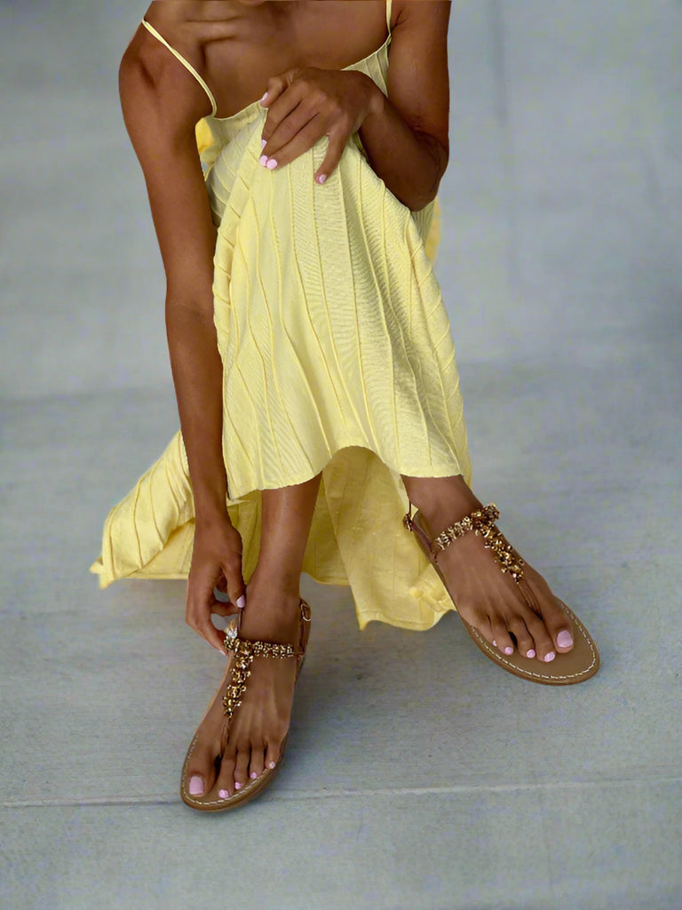 Lady wearing a yellow dress and tan sparkly crystal embellished sandals on a white background