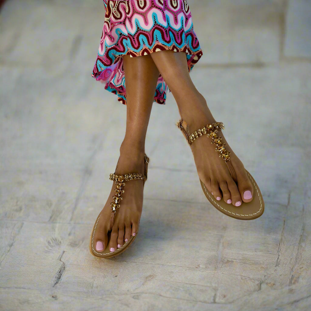 Tan sandals with tan sparkly crystal embellishments worn with a colorful dress on a white background