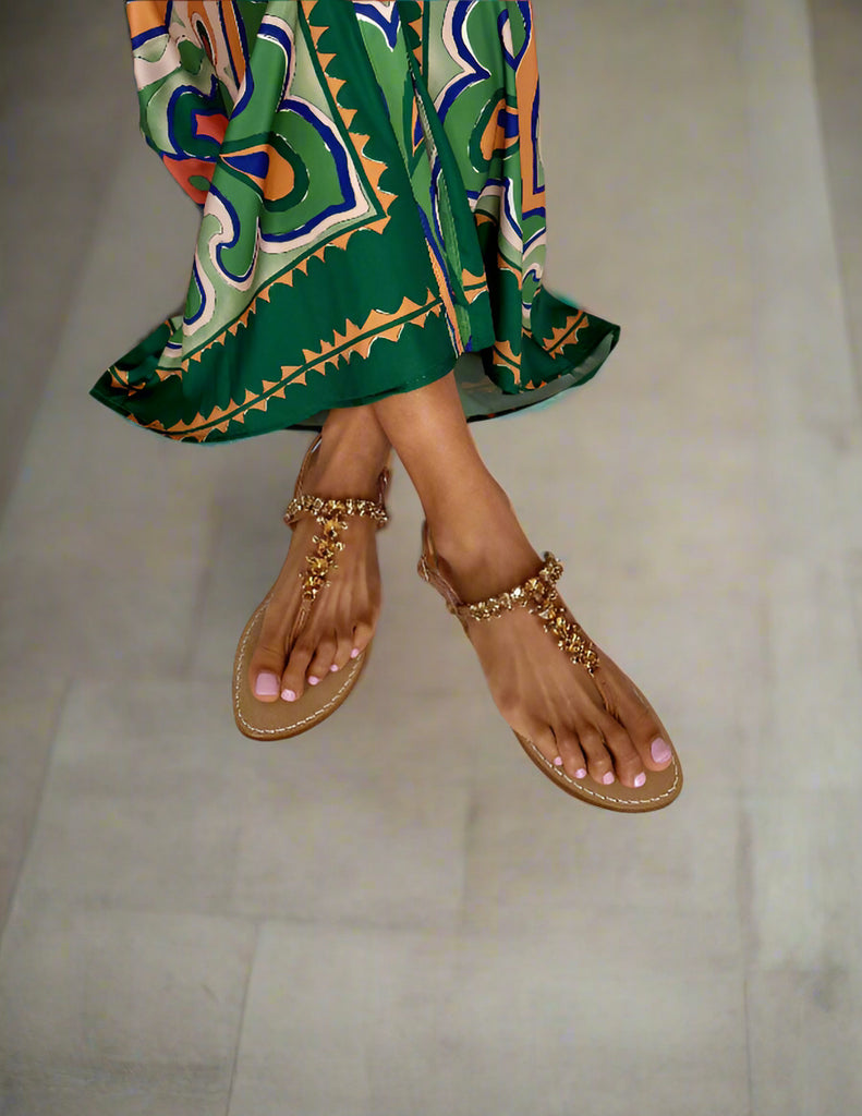 Lady wearing tan sandalswith tan sparkly embellishments and a colourful patterned green dress on a white background