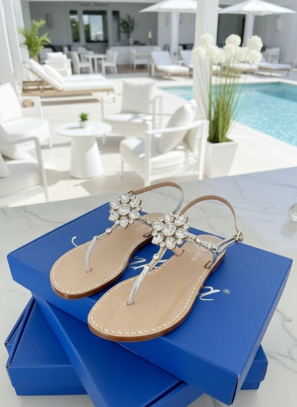 Pair of silver sandals with Swarovski crystal embellishments on luxury blue boxes.