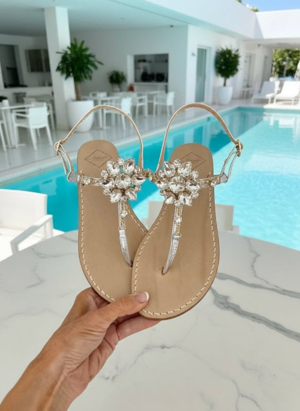 Luxury silver Swarovski crystal sandals held by a hand near a pool.